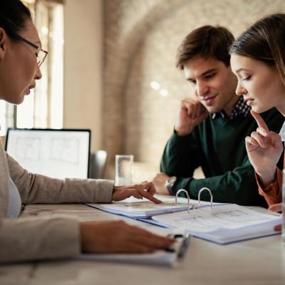Young Man His Wife Examining Housing Plans With Real Estate Agent Meeting Office